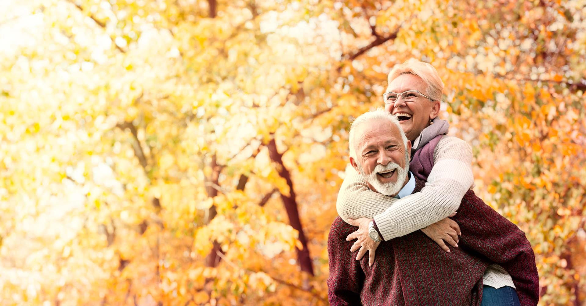 retired couple in front of trees with yellow leaves during fall